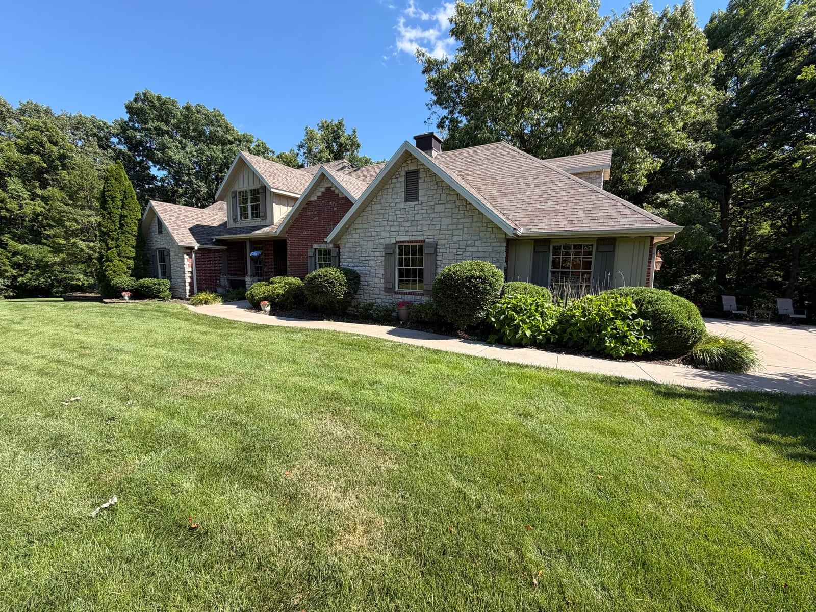 Carefully shaped shrubs and a maintained lawn surrounding a stone and brick home